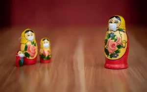 Four colourful Russian nesting dolls wearing face masks, with one doll separated from the others