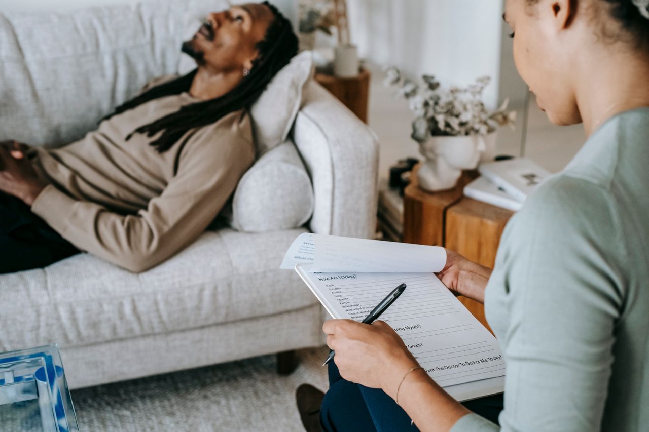 Crop anonymous African American female with paper form talking to male partner during psychotherapy in living room